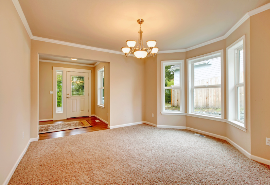 Spacious living room with beige carpet, large bay windows, hardwood flooring in the entryway, and a front door